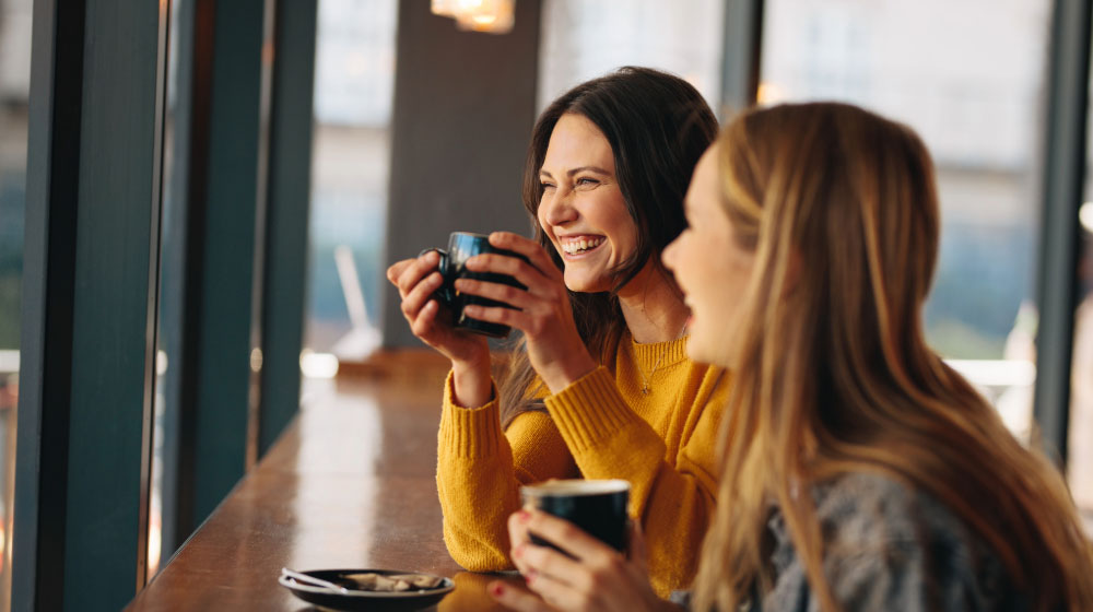 Two women laughing over coffee at a café table